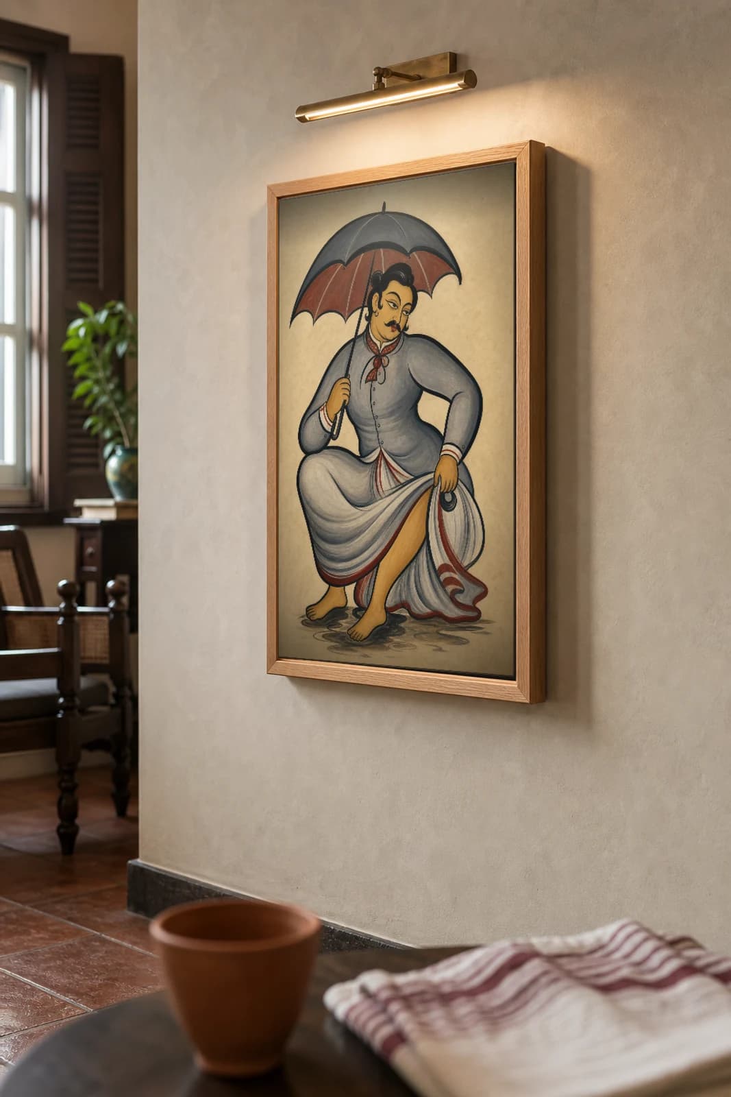 Babu in the Rain Kalighat Print — the dandy crouches under an umbrella lifting his dhoti from the puddles, 19th-century Bengal patua satire, hand-numbered collector edition — the framed print shown at a three-quarter angle on a styled gallery wall in a natural-oak frame