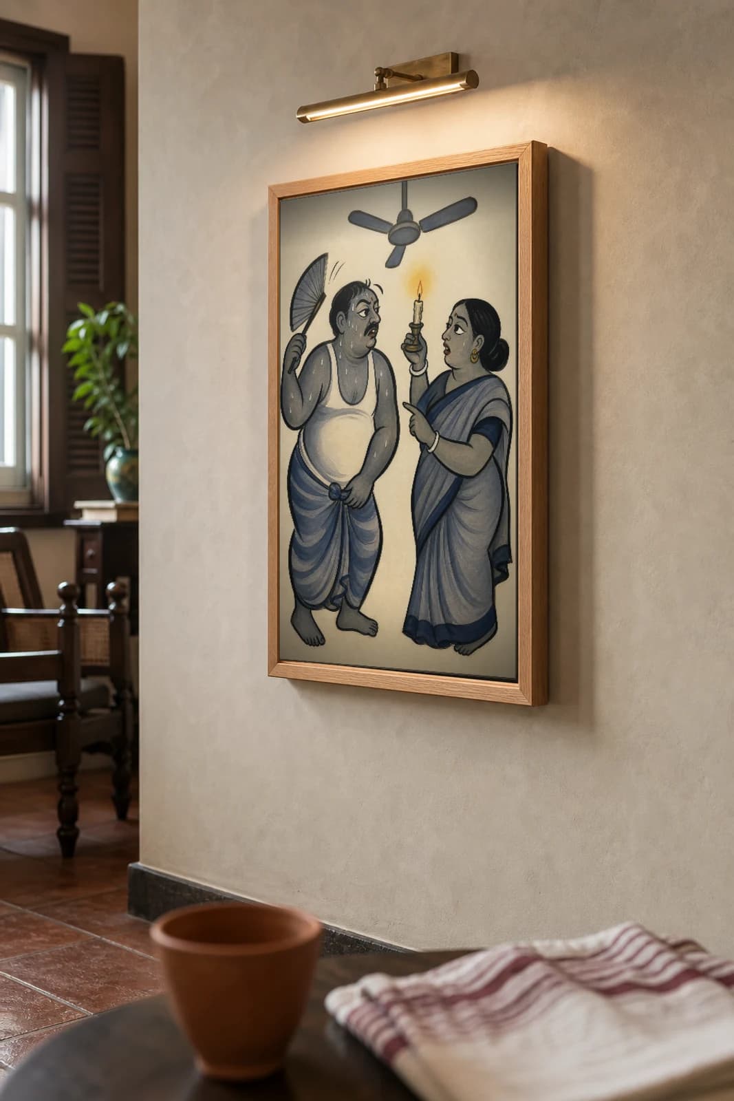 The Load-Shedding — Kalighat-style art print of a sweating household under a dead ceiling fan, Bengal patua brush · collector edition · framed A2 — the framed print shown at a three-quarter angle on a styled gallery wall in a natural-oak frame