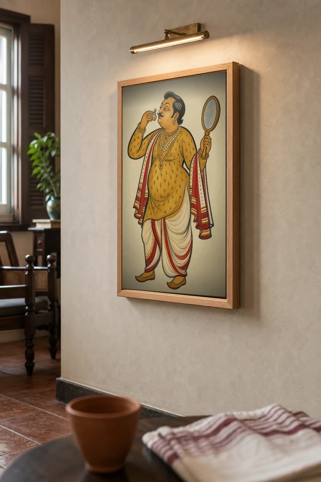 The Biye-Bari Show-Off — Kalighat-style art print of a gold-draped dandy preening for the wedding, Bengal patua brush · collector edition · framed A2 — the framed print shown at a three-quarter angle on a styled gallery wall in a natural-oak frame