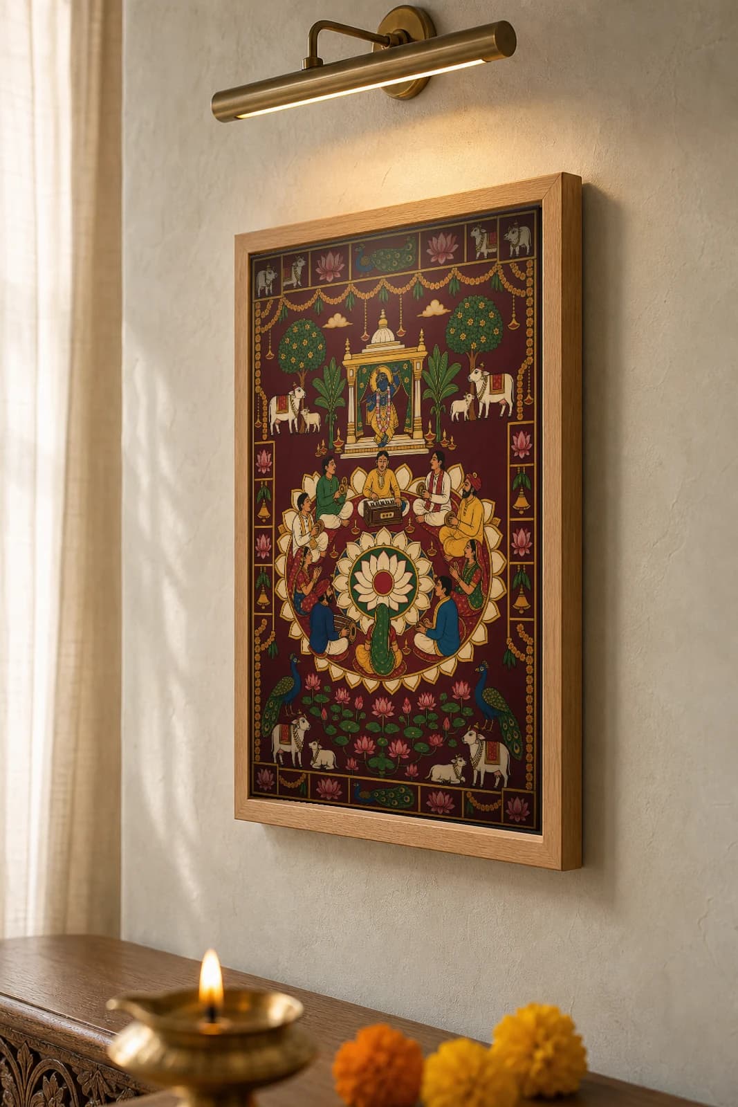 Bhajan Mandali Evening Pichwai-Style Print — a ring of singers and players around a harmonium on a lotus mandala, Shrinathji's shrine above, on deep maroon cloth — the framed print shown at a three-quarter angle on a styled gallery wall in a natural-oak frame