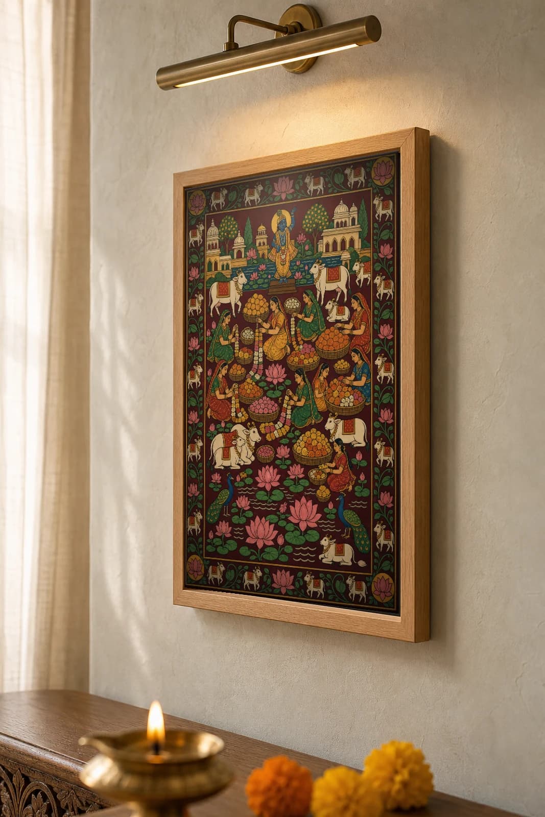 Phool Mandi Pichwai-Style Print — women weaving marigold garlands among baskets of flowers below a Krishna shrine, with cows, peacocks and a lotus pond, on deep maroon cloth — the framed print shown at a three-quarter angle on a styled gallery wall in a natural-oak frame